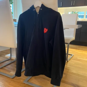 Svart hoodie från Comme des Garçons - Säljer en svart hoodie från Comme des Garçons med det ikoniska röda hjärtat på bröstet fast en annan modell med dubbla hjärtan. Den har en dragkedja framtill och är i storlek L. Perfekt för en stilren och bekväm look. Bara att kontakta mig vid frågor!