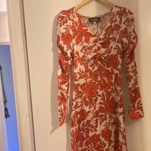 Blommig långklänning från Positano Indiska  - Säljer en superfin långklänning från Positano med ett rött blommigt mönster på vit bakgrund. Klänningen har långa ärmar och en v-ringad design som ger en elegant look. Perfekt för vår och sommarens fester! 🌸