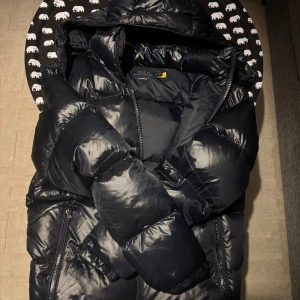 Blå pufferjacka från Polo Ralph Lauren - Säljer en snygg blå pufferjacka från Polo Ralph Lauren i storlek M. Jackan är perfekt för vintern med sitt varma och vadderade material. Den har en dragkedja framtill och en praktisk huva. Jackan är i mycket bra skick och redo för kalla dagar!💙