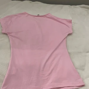 Rosa t-shirt från Elin L - Säljer en söt rosa t-shirt från Elin L i storlek XS. Den är kortärmad och gjord i mjukt bomullsmaterial, perfekt för sommardagar. T-shirten har en enkel och stilren design som passar till det mesta. Perfekt för en avslappnad look! 🌸