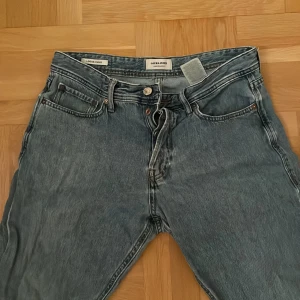 Blå jeans från Jack & Jones - Säljer ett par klassiska blå jeans från Jack & Jones i storlek 31/32. De har en snygg, lite sliten look och är perfekta för vardagsbruk. Jeansen har en normal passform med fem fickor och knappgylf. Perfekta för både höst och vår!