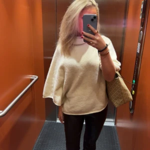 Beige stickad poncho - Funderar på att sälja min supermysiga beiga stickade poncho med hög krage. Perfekt för höst och vinter, den är både stilren och bekväm. Passar bra till både vardag och lite finare tillfällen. Den har en loose passform som gör den extra skön att bära.