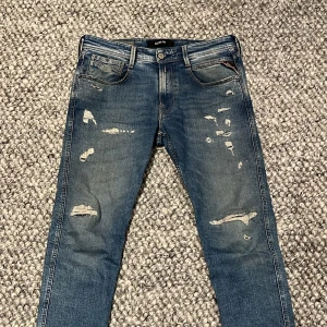 Replay Anbass - Säljer ett par snygga blå jeans från Replay med coola slitningar för en trendig look. De har en klassisk femficksdesign och en bekväm passform. Perfekta för både vardag och fest! 🕺köpte dem för 1799kr på NK🙌🏾