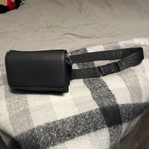 Svart axelväska med justerbar rem - Snygg svart axelväska i skinn med justerbar rem och flera fack. Perfekt för både vardag och fest! Väskan har en praktisk dragkedja och en stilren design. Passar till alla outfits och är i mycket bra skick.💕