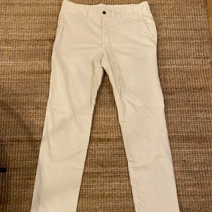 Beige chinos från Tiger of Sweden - Säljer ett par stilrena beige chinos från Tiger of Sweden i storlek 52. De är i mycket bra skick och perfekta för både vardag och fest. Byxorna har en normal passform med knappar och dragkedja i midjan. De är tillverkade i ett mjukt bomullsmaterial som gör dem bekväma att bära hela dagen.