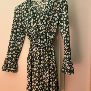 Grön blommig klänning från Shein - Säljer en superfin grön klänning med vita blommor från Shein. Den har långa ärmar och ett knytband i midjan för en snygg passform. Perfekt för vår och sommar! 🌸