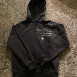 Svart hoodie med Pop Smoke-tryck - Säljer en svart hoodie med tryck av Pop Smoke på både fram- och baksidan. Hoodien har en klassisk design med känguruficka och justerbar huva med snören. Perfekt för fans av Pop Smoke.
