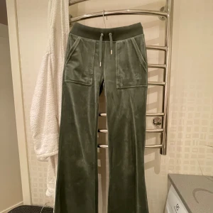 Gröna mjukisbyxor från Juicy Couture - Snygga gröna mjukisbyxor från Juicy Couture med breda ben och snörning i midjan. Byxorna har praktiska fickor både fram och bak med knappar. Perfekta för en avslappnad stil. Köpa för 1200kr