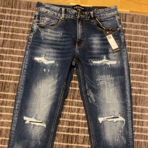 Blå jeans från Supply & Demand - Snygga blå jeans med slitna detaljer från Supply & Demand. De har en slim fit passform och klassisk femficksdesign. Perfekta för en trendig look. Passar även M, köpte den men den passa inte och rev kvittot så kan inte lämna den pris kan diskuteras