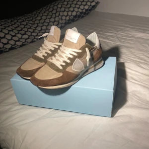 Beige och bruna sneakers från Philippe Model - Snygga sneakers från Philippe Model i beige och brunt. Skorna har en klassisk design med snörning och är tillverkade i mocka och skinn. Perfekta för en stilren look. Skorna är i mycket bra skick. Bara hör av er vid frågor och funderingar!