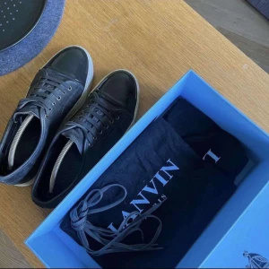 Grå sneakers från Lanvin - Grå sneakers från Lanvin med glansig tå och snörning. Skorna har en vit sula och är tillverkade i skinn och syntetmaterial. Perfekta för en stilren look.