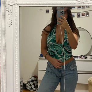 Grön mönstrad topp från Bik Bok - Säljer en snygg grön topp från Bik Bok med ett unikt mönster i svart och vitt. Toppen är ärmlös och har en djup v-ringning. Perfekt för att ge en stilfull touch till din outfit. Storlek XS men passar även till S och M då jag annars brukar ha de