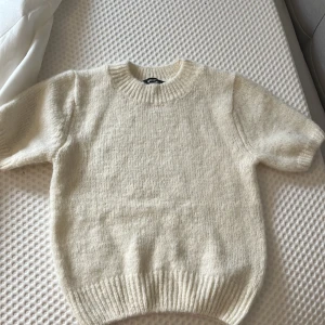 Beige stickad tröja från Gina Tricot  - Mysig vit stickad tröja från Gina Tricot. Tröjan har korta ärmar och ribbade muddar vid ärmslut och nederkant. Perfekt för kyliga dagar. 