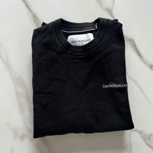 Svart tröja från Calvin Klein Jeans - Säljer en stilren svart tröja från Calvin Klein Jeans. Tröjan har en diskret logga på bröstet och är tillverkad i ett mjukt material. Perfekt för en minimalistisk look.