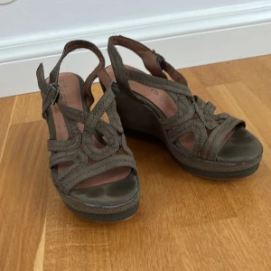 Gröna sandalklackar från Tamaris - Snygga gröna högklackade sandaler i storlek 36 från Tamaris. De har ett flätat mönster och justerbara remmar för perfekt passform. Perfekta för sommarens alla tillfällen. Dem är använda men fortfarande i bra skick! Skriv om du har fler frågor!