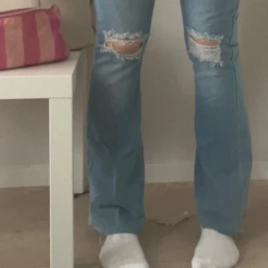 Blå jeans med slitningar - Snygga blå jeans med slitningar på knäna och fransiga kanter. De har en bootcut-stil som ger en avslappnad look. Perfekta för en trendig vardagsstil. Mått: innerbenslängd ~72cm midjemått ~33x2 cm