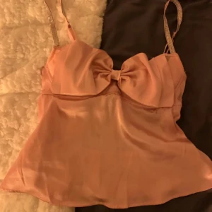 Festlinne - Säljer en söt rosa tubtopp i satin med en stor rosett framtill. Toppen har smala axelband och en glansig finish som ger en lyxig känsla. Fin med lite öppenrygg, perfekt för en kväll ute eller en speciell tillställning. 