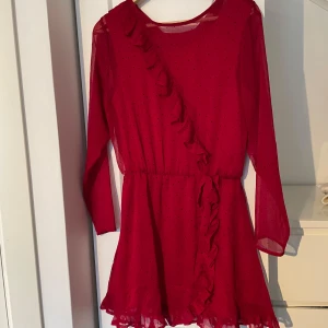 Röd klänning från Grunt - Säljer en röd klänning från Grunt i storlek XL. Klänningen har ett prickigt mönster och volangdetaljer framtill. Den är långärmad och har en luftig passform, perfekt för både vardag och festliga tillfällen.