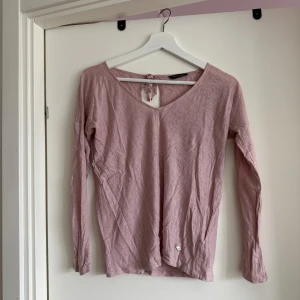Rosa tröja från Massimo Dutti - Säljer en söt rosa tröja från Massimo Dutti med v-ringning och knytning i ryggen. Tröjan har långa ärmar och en liten metalllogga framtill. Perfekt för en stilren look!