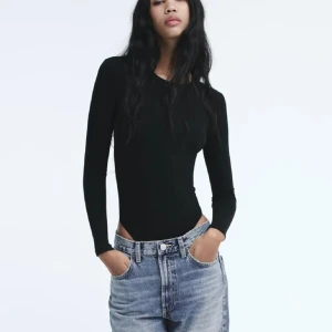 Svart långärmad Zara body - Snygg och stilren svart långärmad topp som passar perfekt till jeans eller kjol. Toppen har en tight passform och är tillverkad i ett mjukt material som ger en bekväm känsla hela dagen.