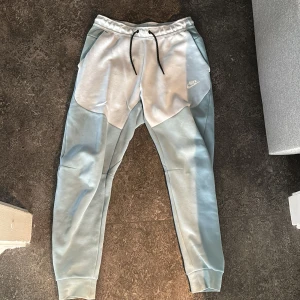 Ljusblå mjukisbyxor från Nike - Snygga ljusblå mjukisbyxor från Nike med elastisk midja och svarta snören. Byxorna har en avslappnad passform och är perfekta för en bekväm stil. De har fickor på sidorna och en liten Nike-logga på framsidan.