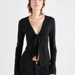 Svart långärmad knytblus - Snygg svart långärmad blus med knytning framtill. Perfekt för en stilren look. Blusen har en djup v-ringning och är tillverkad i ett mjukt material.