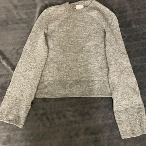 Grå stickad tröja - Säljer en stilren grå stickad tröja med långa ärmar och ribbade detaljer vid ärmslut och nederkant. Enkel att matcha med olika outfits.