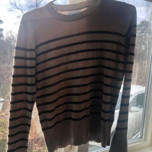 Beige och svart randig tröja från Holly & Whyte - Säljer en stilren beige tröja med svarta ränder från Holly & Whyte by Lindex. Tröjan har långa ärmar och en rund halsringning, perfekt för en avslappnad look. Passar bra till både jeans och kjol. Andvänt några gånger men ser ut som ny❤️