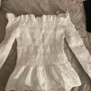 Vit offshoulder volang blus  - Säljer en söt vit offshoulder blus,blusen har volangdetaljer och en smockad design som ger en fin passform. 💗