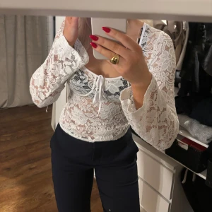 Vit spetsblus från Pieces - Säljer en elegant vit spetsblus från Pieces i storlek m. Blusen har långa ärmar och en knytning framtill som ger en romantisk touch. Perfekt för att lyfta vilken outfit som helst med sin fina spetsdesign.