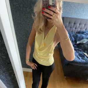 Gul ärmlös topp - Säljer en snygg gul ärmlös topp med djup urringning och öppen rygg. Perfekt för varma dagar eller en utekväll. Toppen har en lös passform som ger en avslappnad och stilren look.