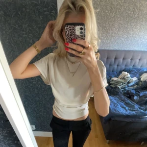 Beige blus med korta ärmar - Säljer en stilren beige blus med korta ärmar och hög krage. Blusen har en elegant passform och är perfekt för en chic look. Liten fläck vid baksida axel, men syns ej tydligt.