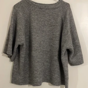 Grå stickad tröja - Mysig grå stickad tröja med trekvartsärm. Perfekt för kyligare dagar och ger en avslappnad look. Passar bra till jeans eller leggings för en casual stil.