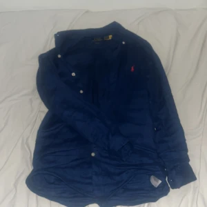 Blå skjorta från Polo Ralph Lauren - Snygg blå skjorta från Polo Ralph Lauren med klassisk krage och knappar framtill. Skjortan har en broderad logotyp på bröstet och är långärmad. Perfekt för en stilren look. Skriv privat för fler bilder