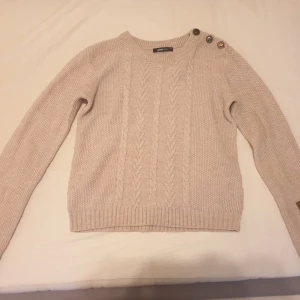 Tröja - Snygg stickad tröja med kabelmönster och bruna detaljer på axlarna och armbågarna. Tröjan har en rund halsringning och är i en ljusrosa färg.säljs för 50