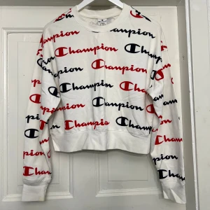 Vit sweatshirt från Champion - Säljer en vit sweatshirt från Champion som är använd ett fåtal gånger. Den har ett all-over tryck med Champion-loggan i rött och svart. Tröjan är långärmad och är i storlek L. Dock passar den också mig som är i storlek S/M. 