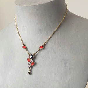 Guldhalsband med röda och lila stenar - Säljer ett elegant guldfärgat halsband från pilgrim med vackra röda och lila stenar.Perfekt för att lyfta vilken outfit som helst, oavsett om det är till fest eller en speciell kväll. 