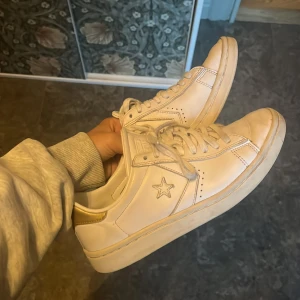 Vita sneakers från Converse - Säljer ett par vita sneakers från Converse. De har en klassisk design med en stjärna på sidan och snörning framtill. Skorna är i syntetmaterial och har en bekväm passform. Perfekta för vardagsbruk och ger en stilren look.