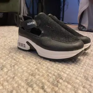 Säljer ett par svarta sneakers med vit sula. De har en cool mesh-design och texten 'FASHION' på sidan. Perfekta för en casual look och superbekväma att gå i. Passar till både vardag och träning!