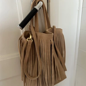 Mini väska i mocca med fransar  - Säljer min trendiga mini väska med fransar i beige/kaki mocca. Köpte i Frankrike i sommras och är helt oanvänd😍