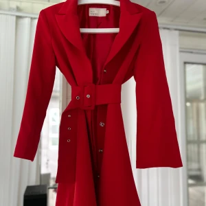 Röd kappa från Silvian Heach - Säljer en superfin röd kappa/klänning i M passar även S. Den har en elegant design med ett bälte i midjan. Perfekt för höst och vinter, och ger en snygg och stilren look. Passar både till vardags och festliga tillfällen!😍