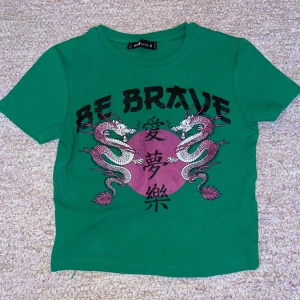 Grön T-shirt med tryck. - Säljer en grön T-shirt med ett häftigt tryck på. Används många gånger men växt ur. Det är i bra skick! Vet ej vad det står, pris kan diskuteras.