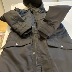 Svart parkajacka från 157 - Säljer en svart parkajacka från 157 i storlek S. Jackan har en mysig fleecefodring och är perfekt för kalla dagar. Den har en dragkedja framtill och praktiska fickor med knappar. Perfekt för höst och vinter!