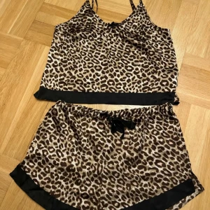 Leopardmönstrad pyjamas i satin - Säljer en superfin leopardmönstrad pyjamas i satin. Setet består av en ärmlös topp med smala reglerbara axelband och matchande shorts. Båda delarna har svarta detaljer vid kanterna. NYTT från Bubbleroom. Storlek M🖤