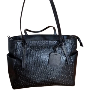 Svart väska från Simmi - En medelstor väska med Steve Madden-loggan präglad i "lädret" (den är tillverkad av PU-läder!).  Väskan har använts mycket men är fortfarande i utmärkt skick, vilket betyder att den kommer att hålla i många år framöver!  Mått: Bredd: 35 cm Höjd: 29 c