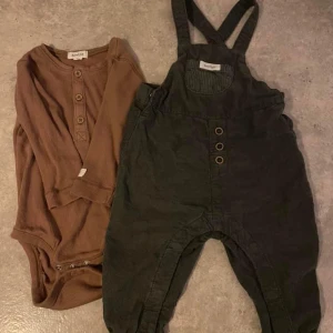 Bruna och gröna barnkläder - Säljer ett set med bruna och gröna barnkläder. Den bruna delen är en ribbad body med knappar framtill, perfekt för höst och vinter. Den gröna delen är ett par hängselbyxor i manchester med knappar, vilket ger en söt och bekväm stil för de små.