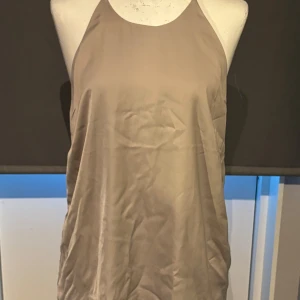 Beige klänning från H&M - Säljer en stilren beige topp från H&M. Den är axelbandslös och har knapp i ryggen för enkel påklädning. Perfekt för både vardag och festliga tillfällen. Klänningen är i ett mjukt och bekvämt material.