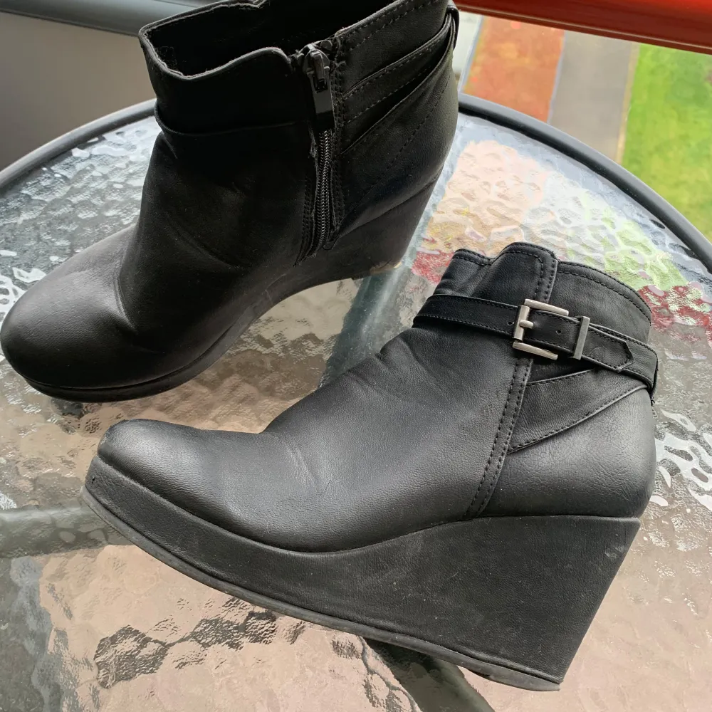 Säljer ett par svarta boots med kilklack från VO Shoes. De har en snygg dragkedja på sidan och ett dekorativt spänne runt ankeln. Perfekta för höst och vinter, och de ger en stilren look till vilken outfit som helst.. Skor.