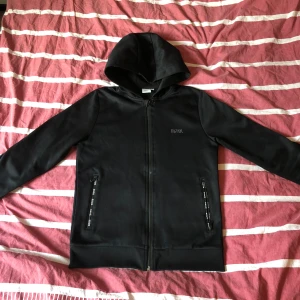 Hugo boss hoodie  - Säljer denna Hugo boss hoodie, den har inga hål och tröjan är i gott skick men det finns ett litet slitage på dragkedjan som syns på bilden. Den är i storlek 150.