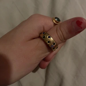 Guldfärgad ring med färgglada stenar - sparsamt använd, har ingen aning om storleken men har väldigt små fingrar och den sitter perfekt på min tumme.